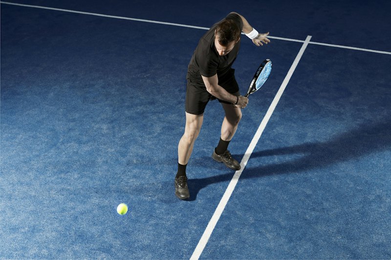 Een speler in zwarte sportkleding buigt diep door zijn knieën om een lage bal te halen.