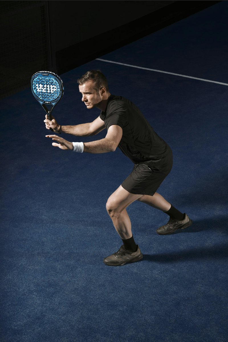 Een speler staat klaar met gebogen knieën en zijn racket voor zich, de blik gericht op de bal.