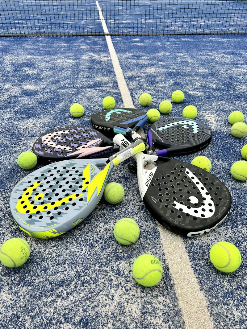 Vier padelrackets in een kring op de baan, omringd door gele ballen.